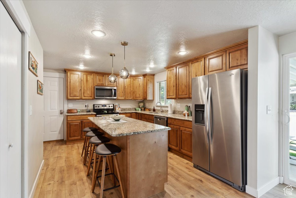 Kitchen with stainless steel appliances, light wood-style flooring, a center island, a breakfast bar, and a textured ceiling