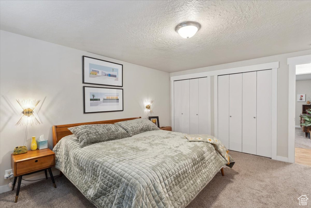 Bedroom with two closets, carpet flooring, baseboards, and a textured ceiling