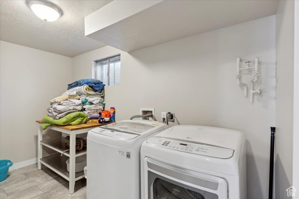 Laundry room featuring washing machine and clothes dryer, a textured ceiling, and baseboards
