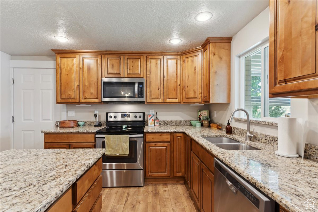 Kitchen featuring stainless steel appliances, a sink, a textured ceiling, light wood-type flooring, and light stone countertops