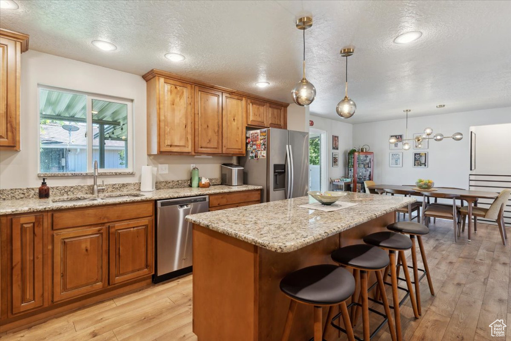 Kitchen with appliances with stainless steel finishes, a sink, light wood-style flooring, a kitchen bar, and a kitchen island