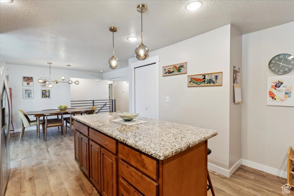 Kitchen featuring light wood-style floors, a textured ceiling, a kitchen island, baseboards, and light stone counters