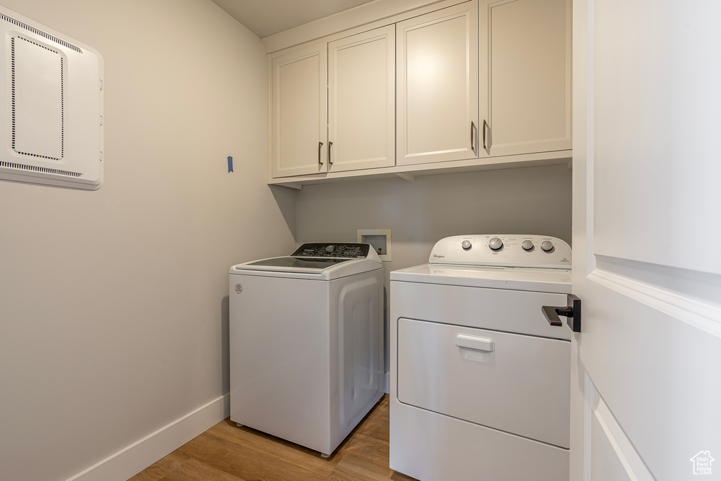 Laundry area featuring separate washer and dryer, cabinet space, light wood-style flooring, and baseboards