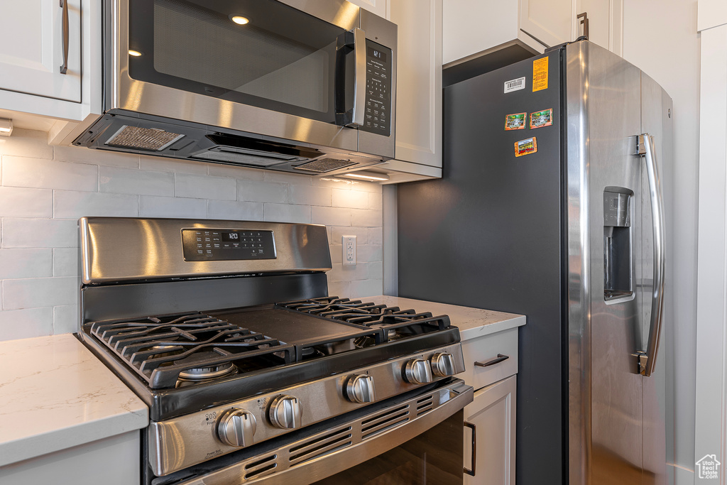 Kitchen with stainless steel appliances, white cabinets, backsplash, and light stone countertops