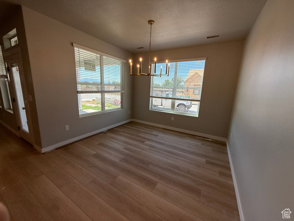 Unfurnished dining area featuring wood finished floors, a chandelier, and baseboards