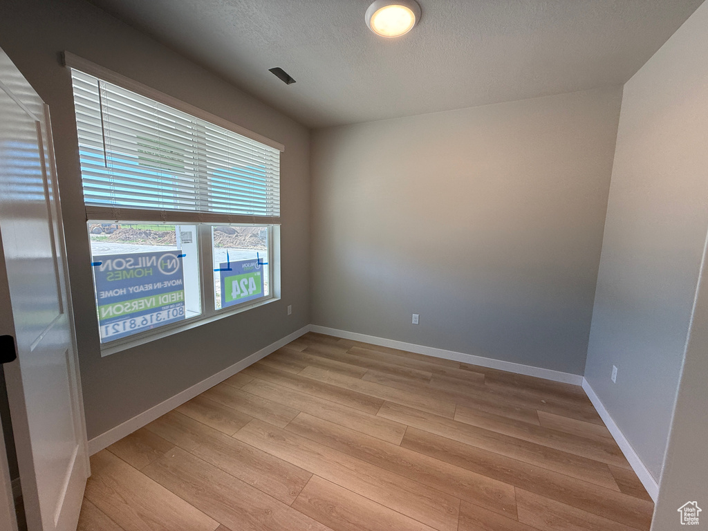 Unfurnished room with light wood-type flooring, baseboards, and a textured ceiling