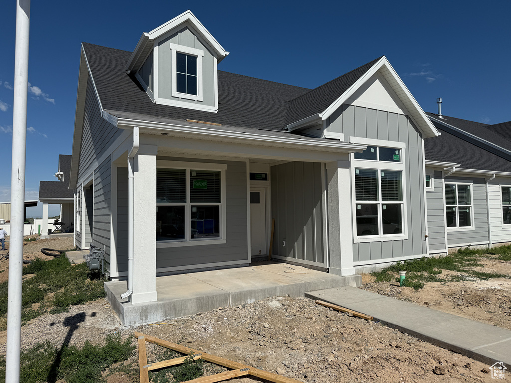 View of front of property with covered porch, roof with shingles, and board and batten siding