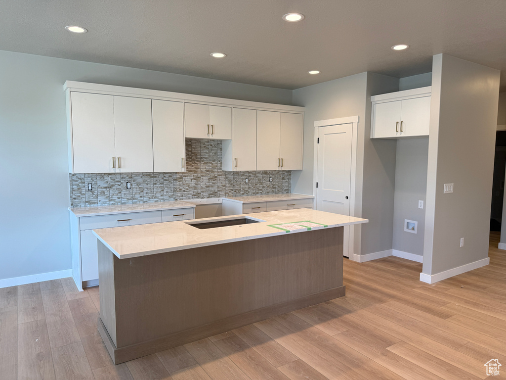 Kitchen with baseboards, backsplash, white cabinets, a kitchen island, and light wood-style floors