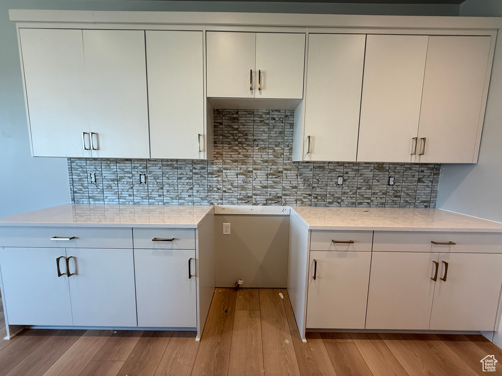 Kitchen featuring light wood-style floors, a sink, decorative backsplash, and white cabinetry