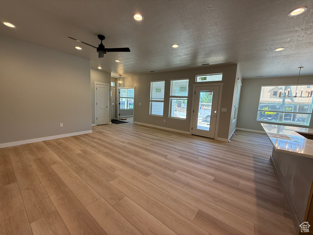 Unfurnished living room featuring baseboards, a textured ceiling, light wood-style flooring, ceiling fan, and recessed lighting