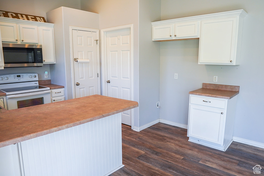 Kitchen with stainless steel microwave, white range with electric cooktop, dark wood-style flooring, white cabinetry, and baseboards