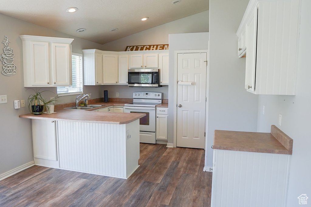 Kitchen featuring white electric range oven, stainless steel microwave, a sink, vaulted ceiling, and a peninsula