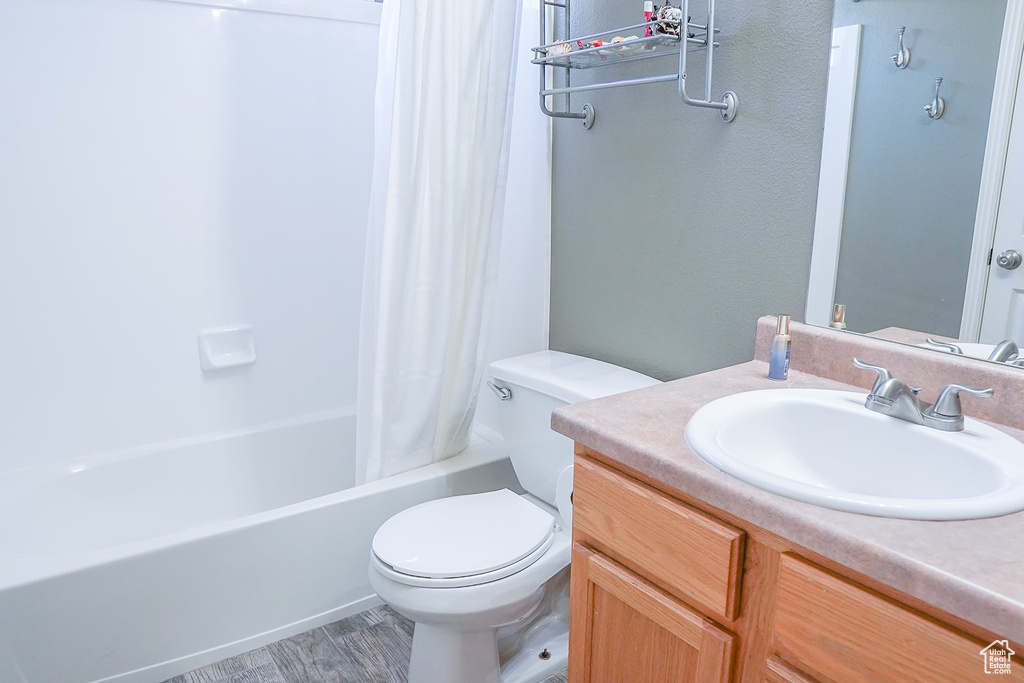 Bathroom featuring toilet, vanity, shower / bathtub combination with curtain, and wood finished floors