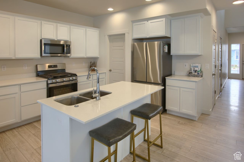 Kitchen featuring stainless steel appliances, a sink, recessed lighting, light wood-style floors, and a breakfast bar