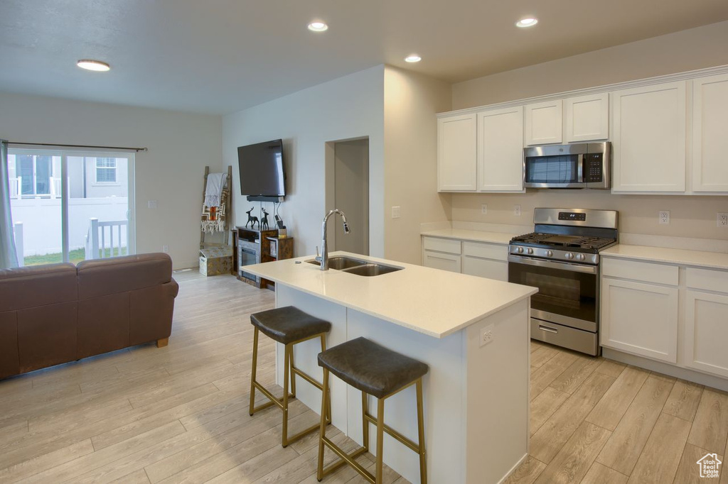 Kitchen with appliances with stainless steel finishes, a sink, open floor plan, light wood finished floors, and white cabinetry
