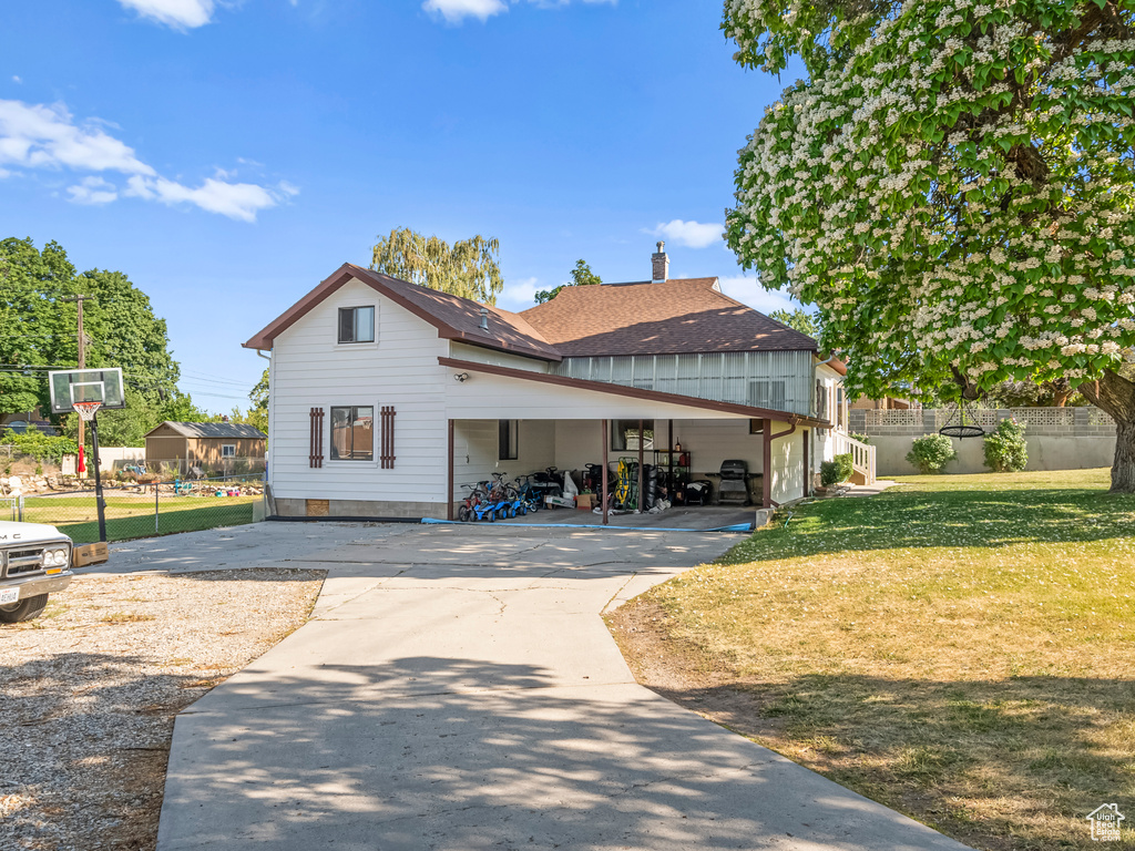 View of front of house featuring concrete driveway, a front lawn, a chimney, a carport, and roof with shingles