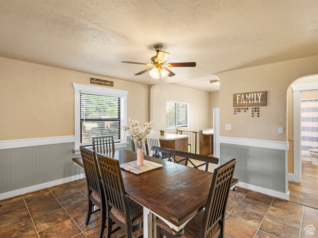 Dining area with a wainscoted wall, a ceiling fan, a textured ceiling, and arched walkways