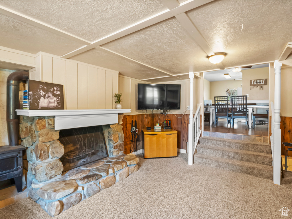 Carpeted living area featuring a textured ceiling, wood walls, a wainscoted wall, a wood stove, and a fireplace