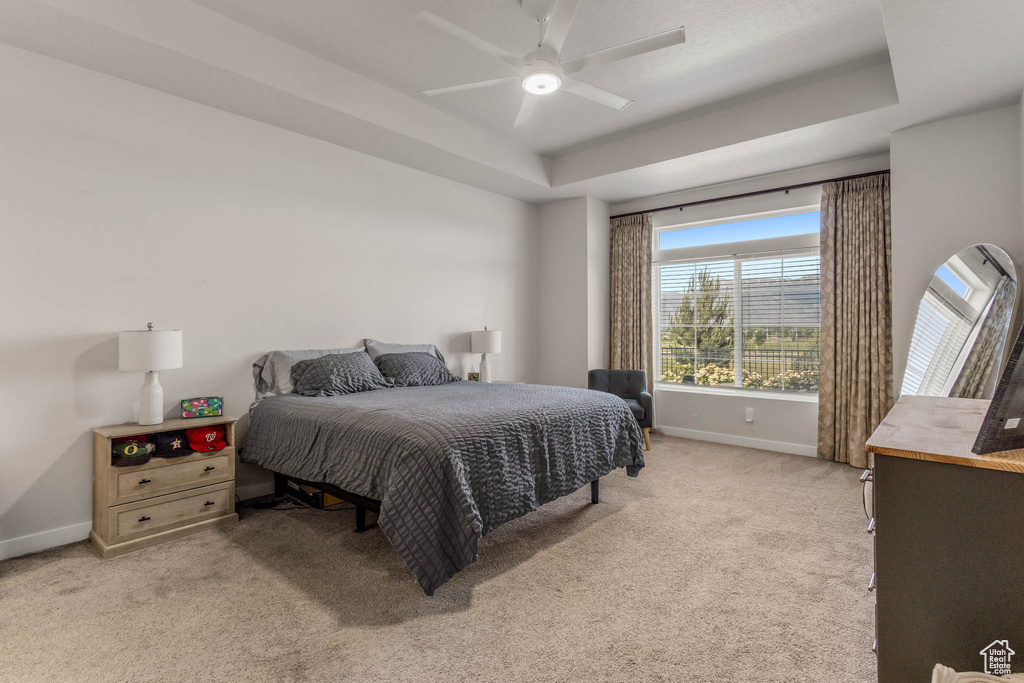 Bedroom with baseboards, light colored carpet, a raised ceiling, and ceiling fan