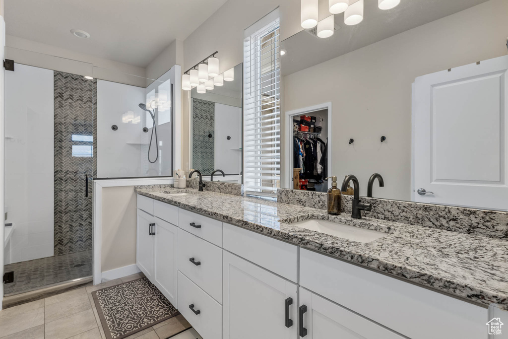 Bathroom with a tile shower, double vanity, a spacious closet, and tile patterned flooring