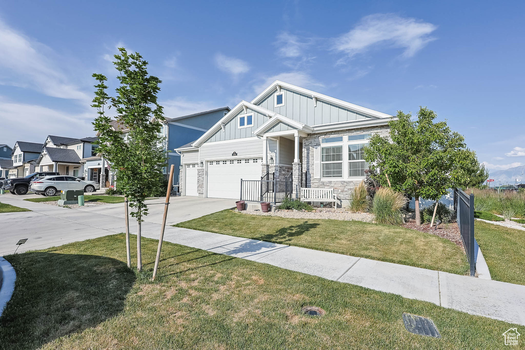 View of front of home with board and batten siding, concrete driveway, a front yard, and stone siding