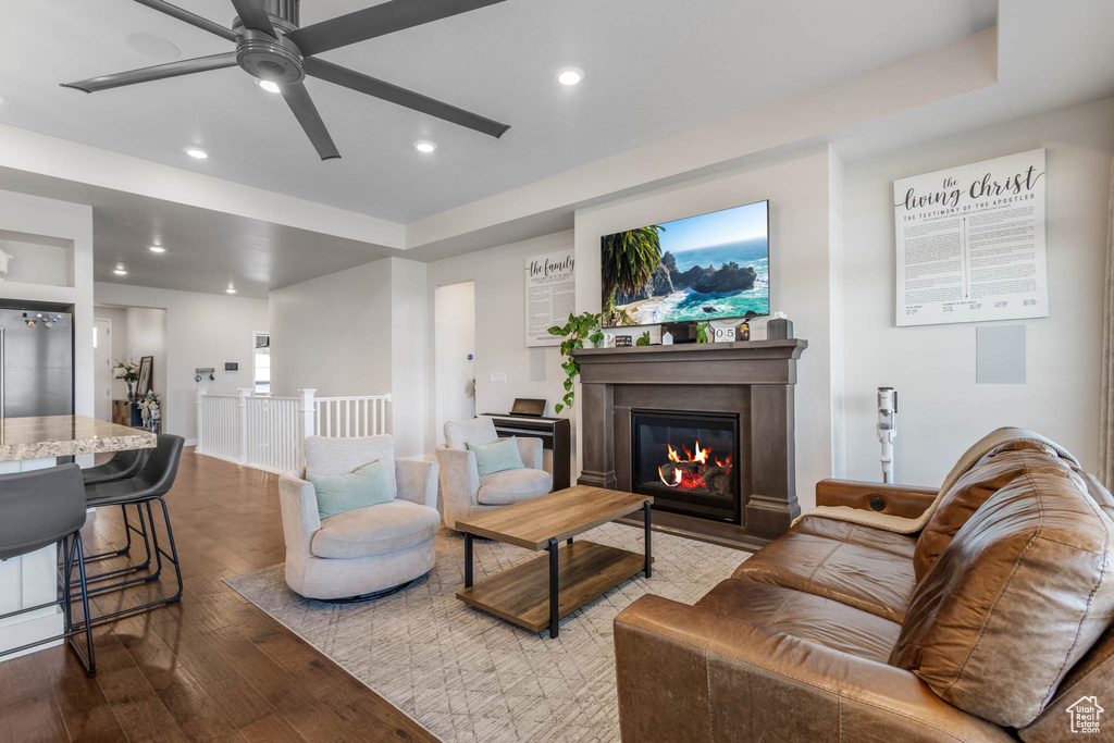 Living room with wood-type flooring, recessed lighting, ceiling fan, a glass covered fireplace, and a raised ceiling