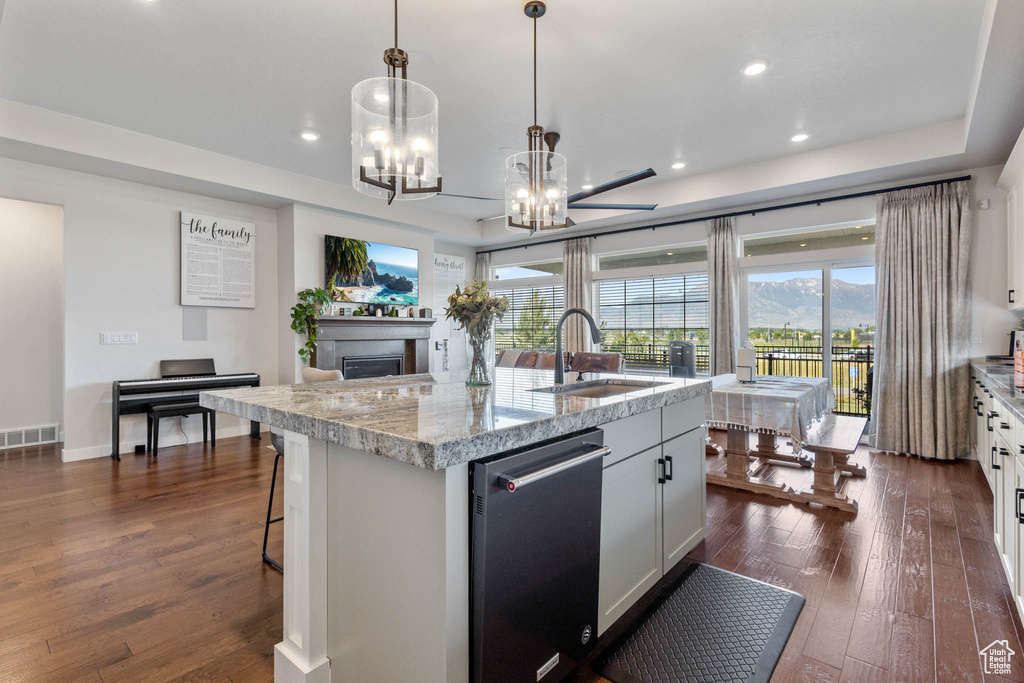 Kitchen with a sink, dishwasher, dark wood-style flooring, a chandelier, and an island with sink