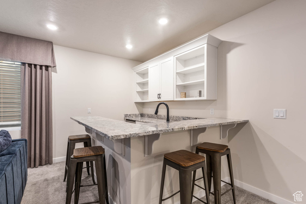 Kitchen featuring open shelves, light carpet, white cabinetry, a kitchen bar, and baseboards