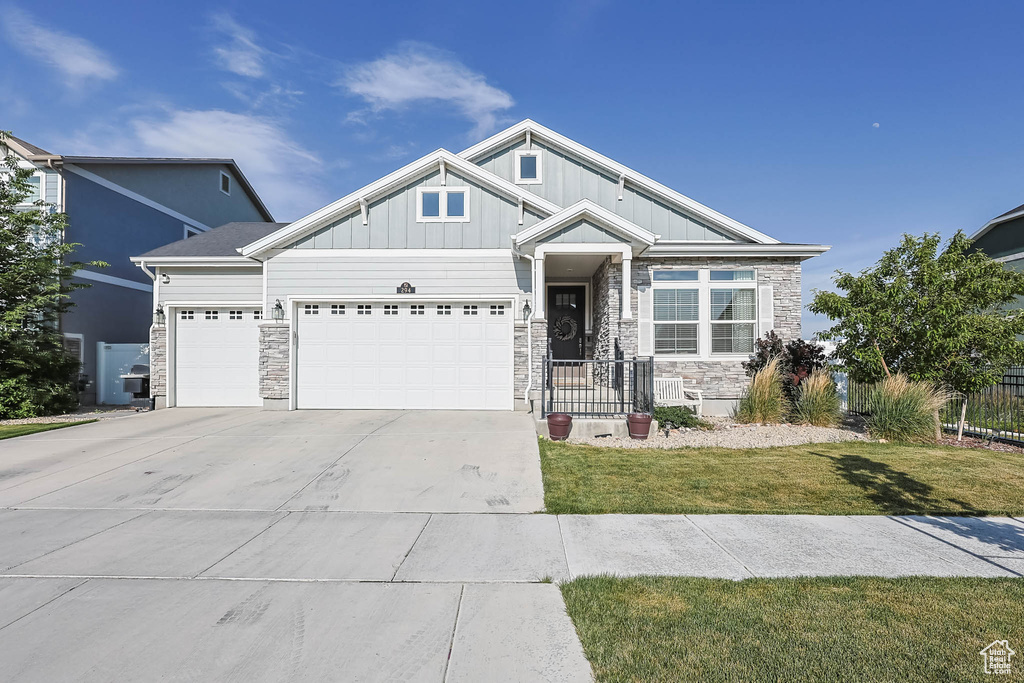 View of front of house with stone siding, an attached garage, concrete driveway, and board and batten siding