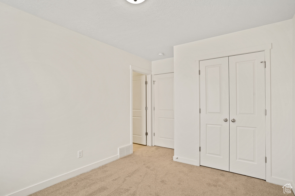 Unfurnished bedroom with light colored carpet, baseboards, and a closet