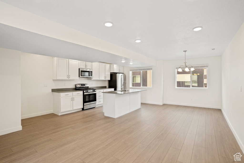 Kitchen with stainless steel appliances, baseboards, a chandelier, white cabinets, and light wood-style floors