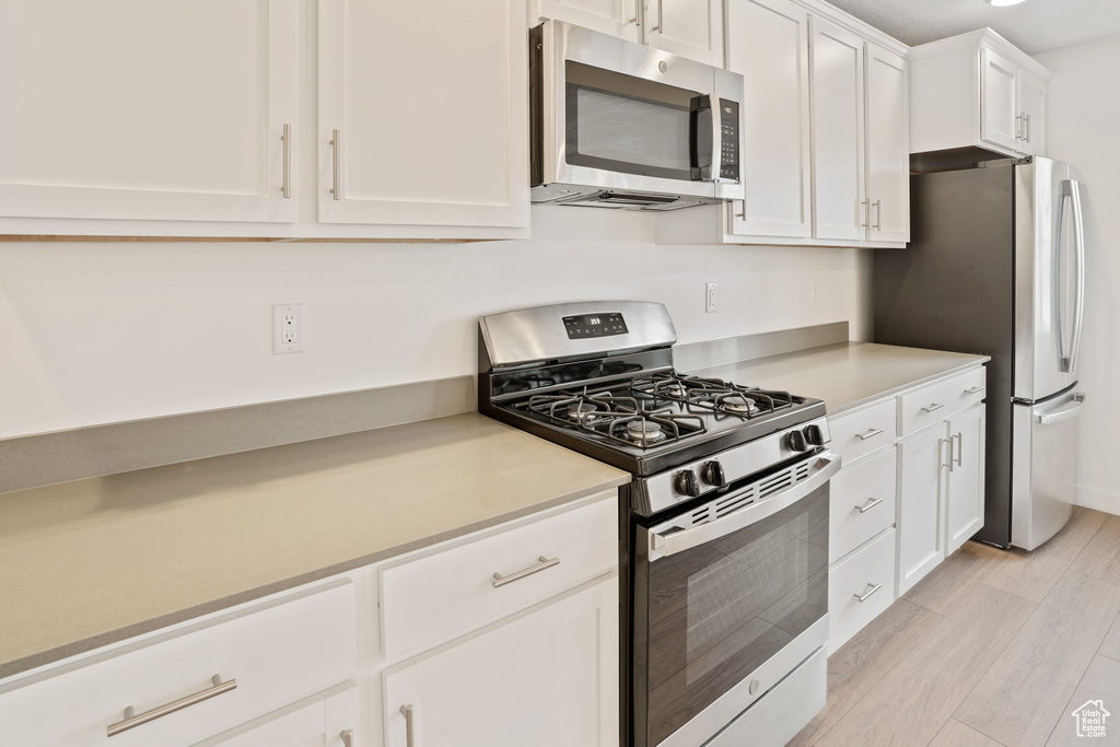 Kitchen featuring appliances with stainless steel finishes, white cabinets, light countertops, and light wood-style floors