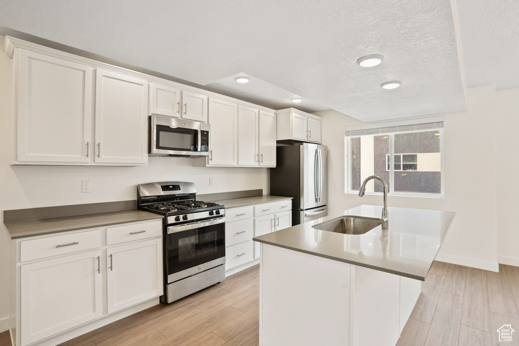 Kitchen featuring appliances with stainless steel finishes, a sink, white cabinetry, light wood-style flooring, and a textured ceiling