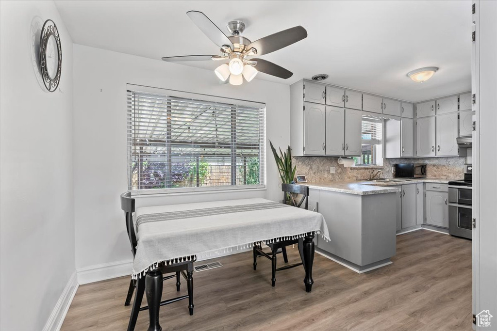 Kitchen featuring stainless steel range with electric stovetop, black microwave, backsplash, light countertops, and a ceiling fan