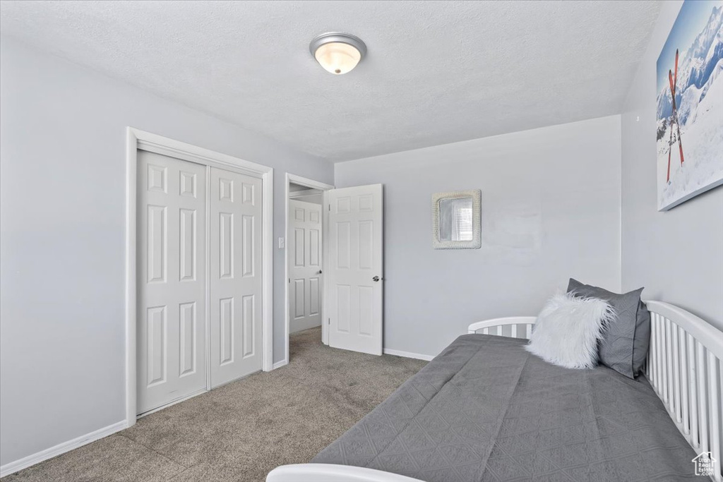 Carpeted bedroom featuring a textured ceiling, a closet, and baseboards