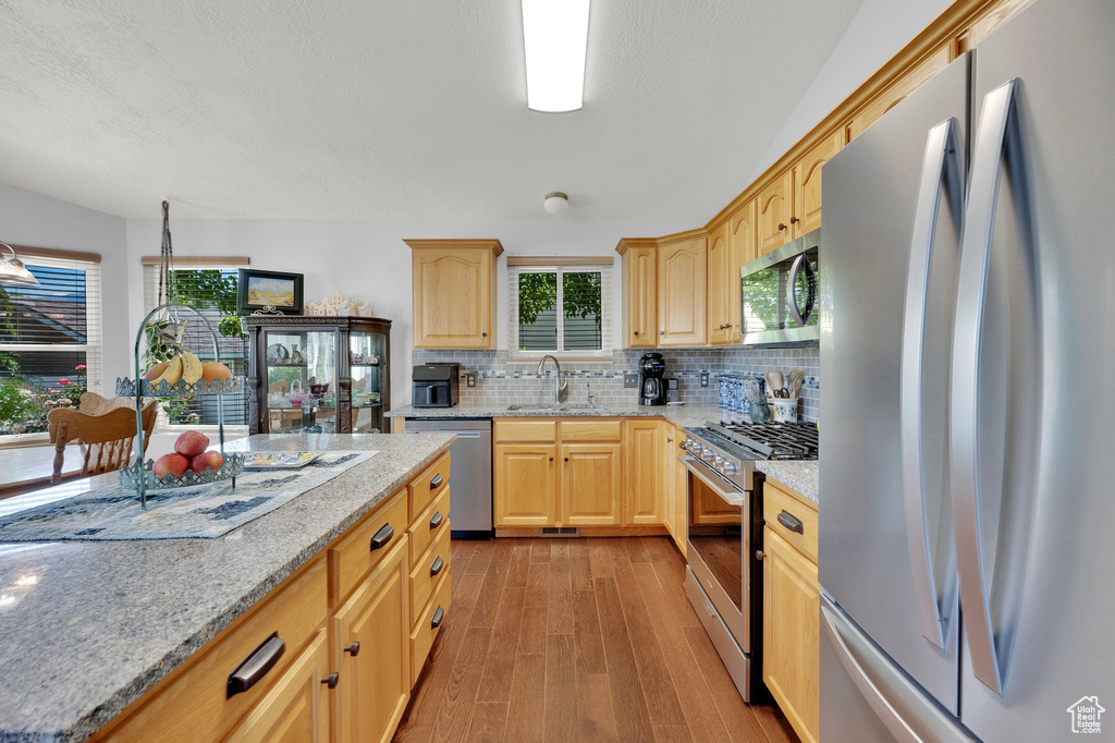 Kitchen with stainless steel appliances, light brown cabinets, light wood finished floors, tasteful backsplash, and light stone counters