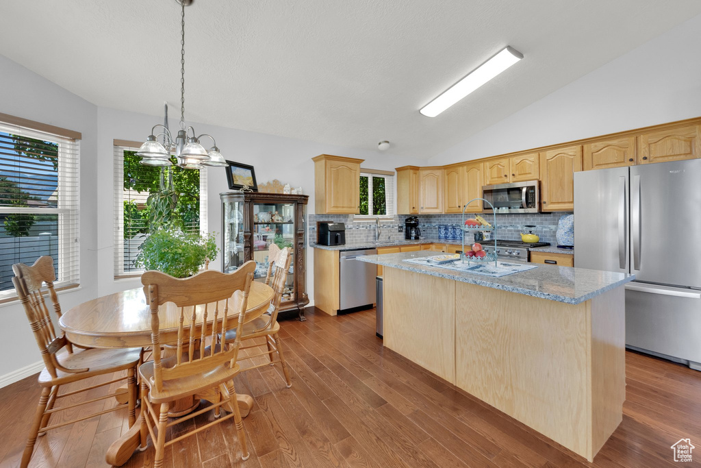 Kitchen featuring appliances with stainless steel finishes, vaulted ceiling, light brown cabinetry, tasteful backsplash, and wood finished floors