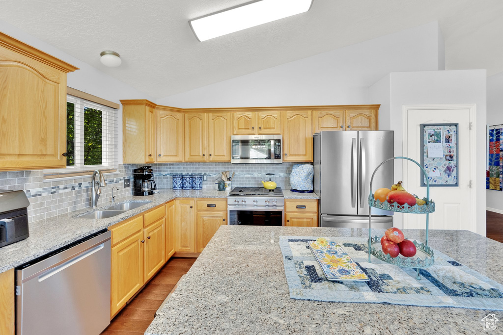 Kitchen featuring appliances with stainless steel finishes, lofted ceiling, light brown cabinets, dark wood-style flooring, and tasteful backsplash