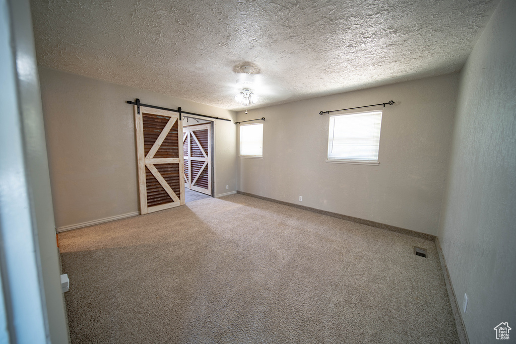 Carpeted spare room featuring a barn door and a textured ceiling