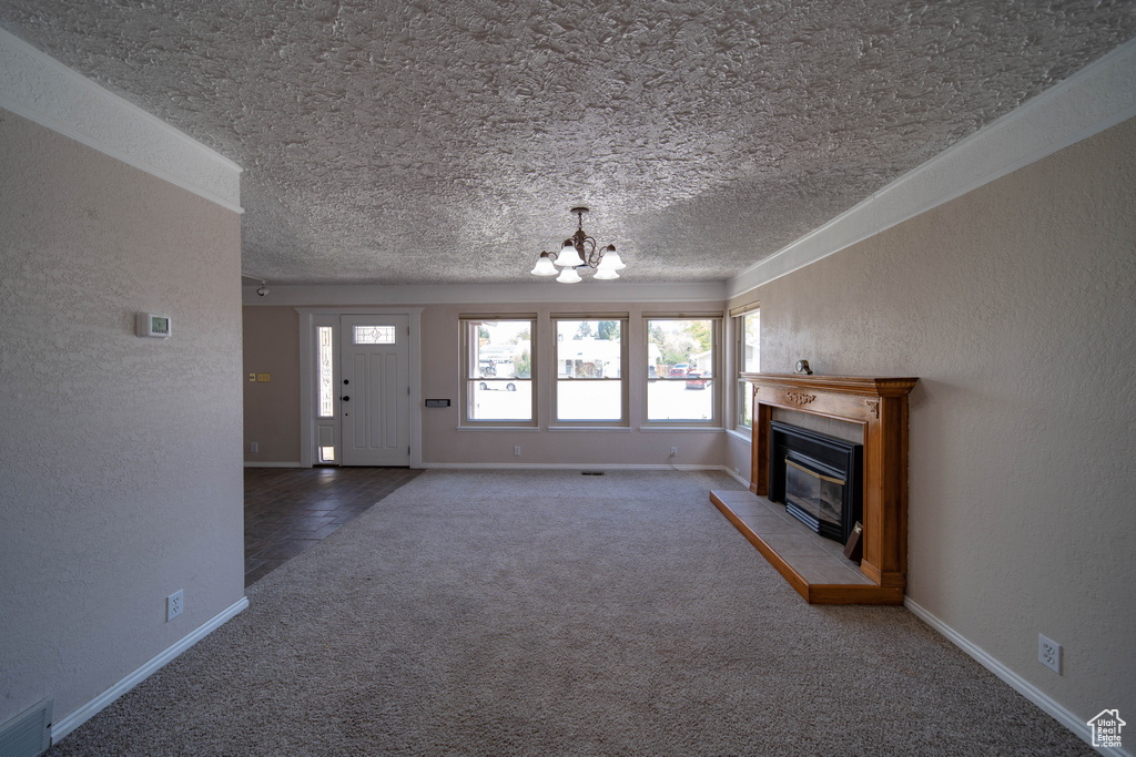 Unfurnished living room with carpet floors, a chandelier, a textured ceiling, plenty of natural light, and a glass covered fireplace