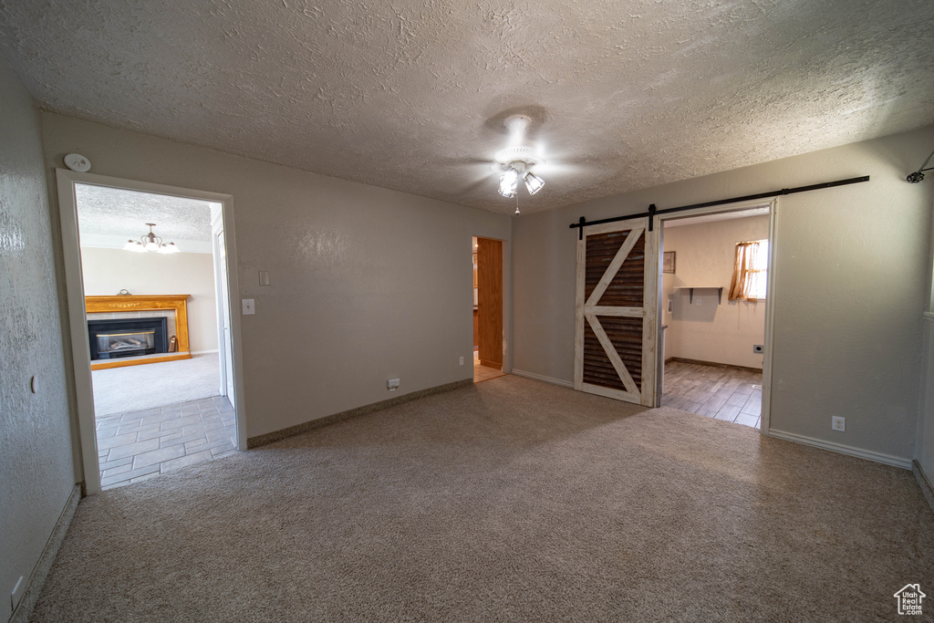 Carpeted empty room with a barn door, a textured ceiling, a chandelier, a glass covered fireplace, and a smoke detector