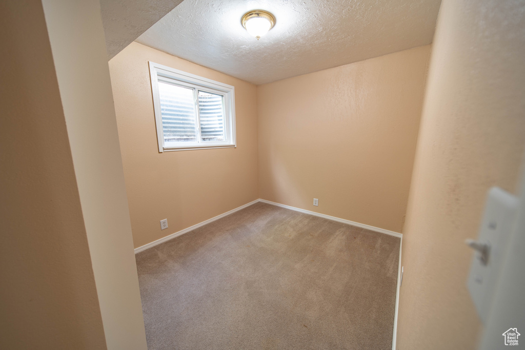 Carpeted empty room featuring a textured ceiling and baseboards