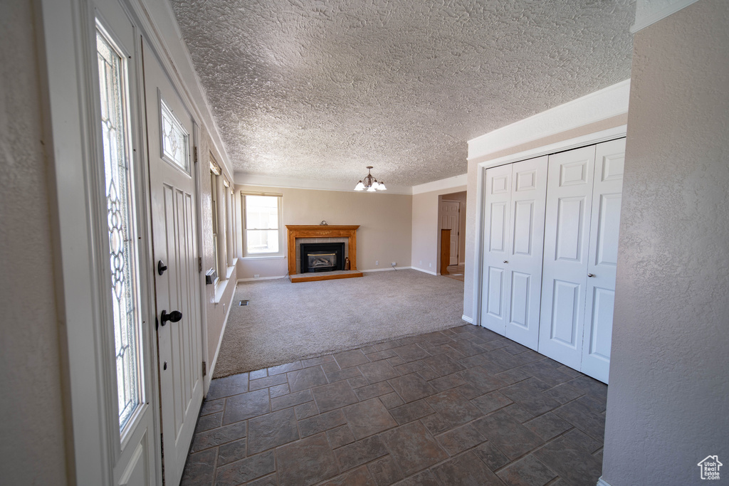 Entryway with dark carpet, dark stone finish floors, a textured ceiling, a chandelier, and a fireplace with raised hearth