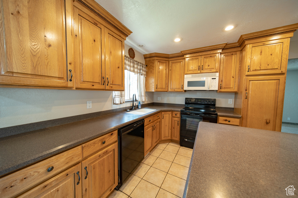 Kitchen featuring black appliances, dark countertops, light tile patterned flooring, recessed lighting, and brown cabinets