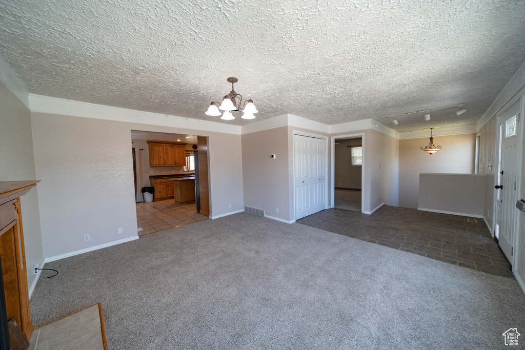 Unfurnished living room with a chandelier, light colored carpet, a textured ceiling, and light tile patterned floors