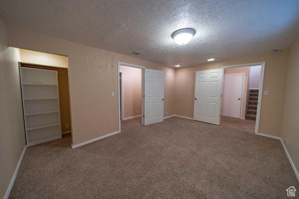 Unfurnished bedroom featuring a textured ceiling, carpet floors, a walk in closet, and a closet