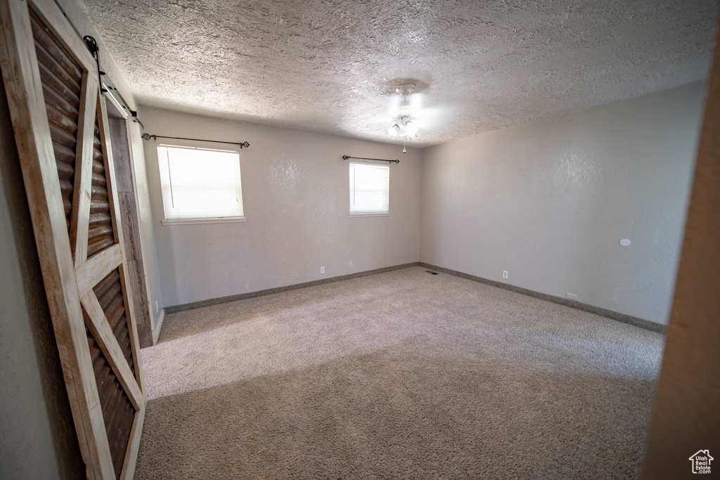 Empty room with a barn door, carpet flooring, and a textured ceiling
