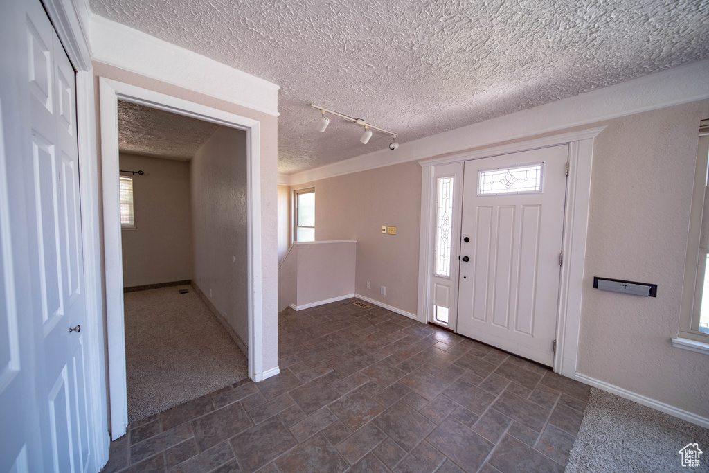 Foyer with a textured ceiling, rail lighting, and dark stone finish floors