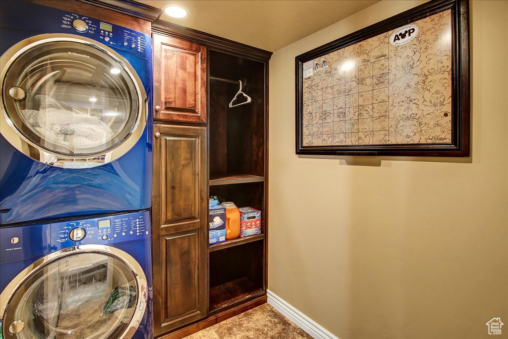 Laundry room featuring stacked washer / drying machine, cabinet space, and baseboards