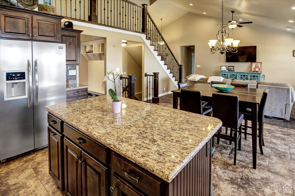 Kitchen featuring stainless steel refrigerator with ice dispenser, light stone counters, open floor plan, a center island, and dark brown cabinetry
